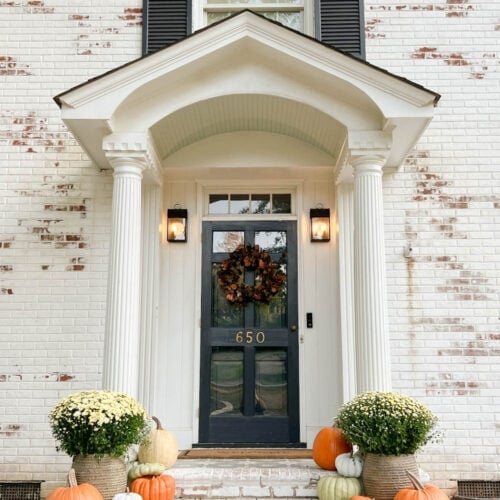 front porch decorated for fall with fake pumpkins and mums on porch steps with limewashed brick