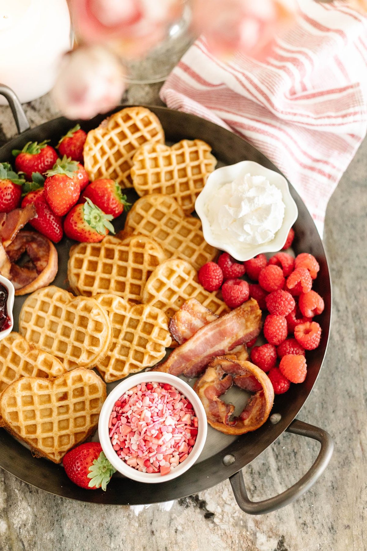 Valentine's Day breakfast charcuterie board with heart shaped waffles, XO bacon, berries, and condiments on a tray