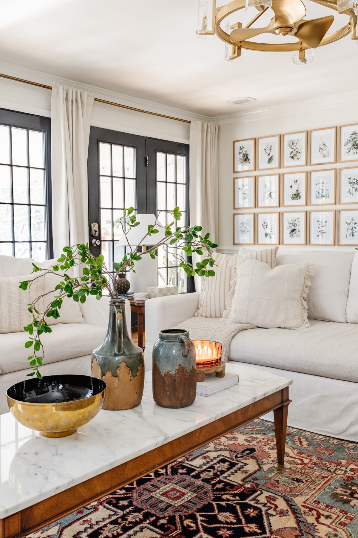 winter living room January decor with white sofas, candle, and vase of greenery on coffee table
