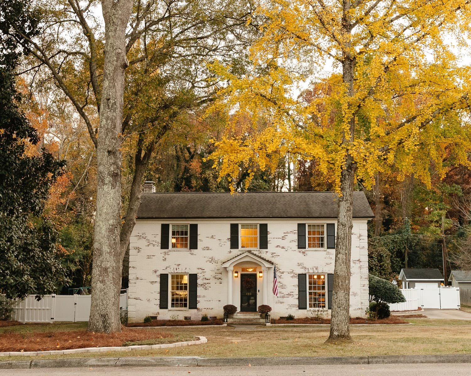limewashed brick colonial house with fall trees