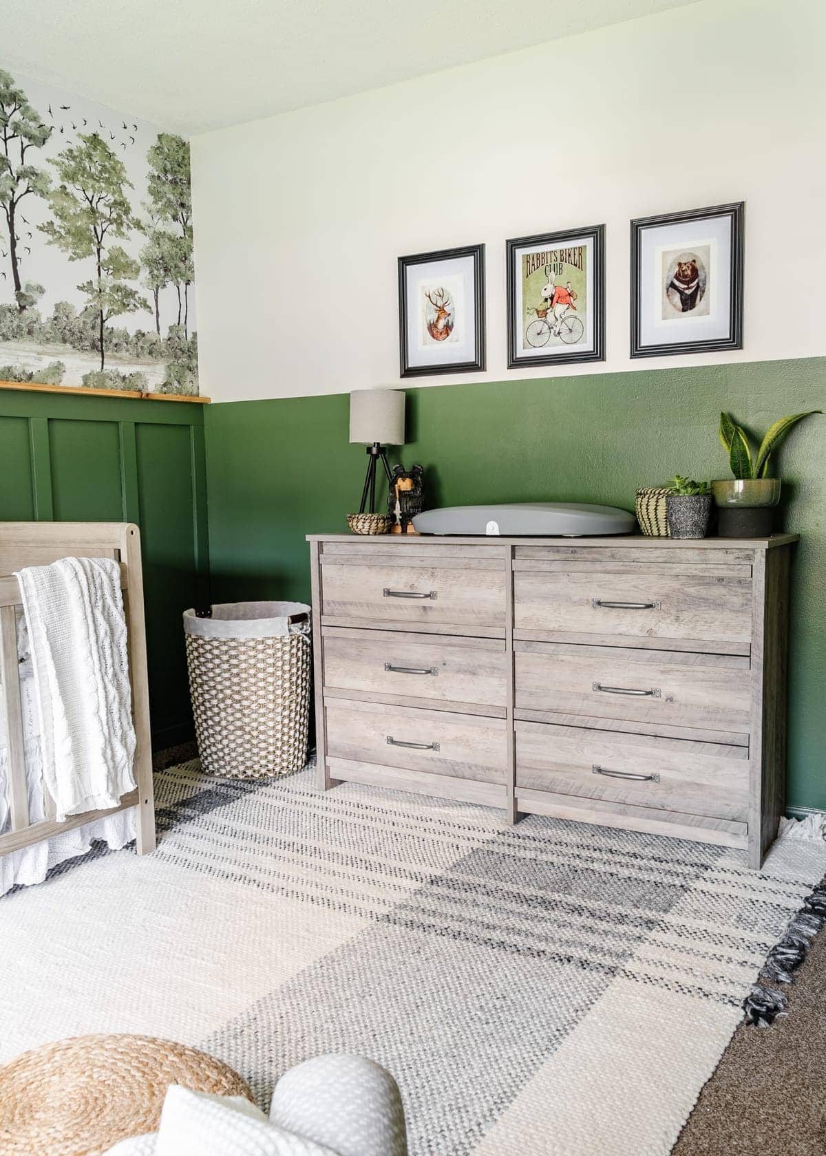 woodland nursery idea using forest wall mural, weathered wood furniture, plaid rug, and woodland animal art