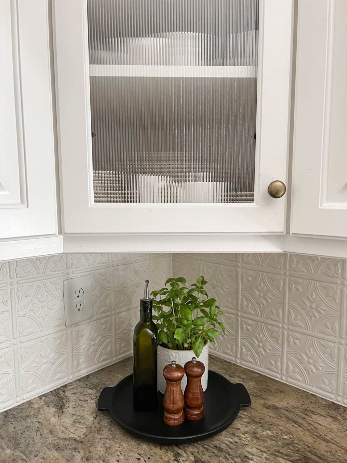 reeded glass cabinet and kitchen countertop decorative tray with potted herbs, bottle of olive oil, and salt and pepper grinders