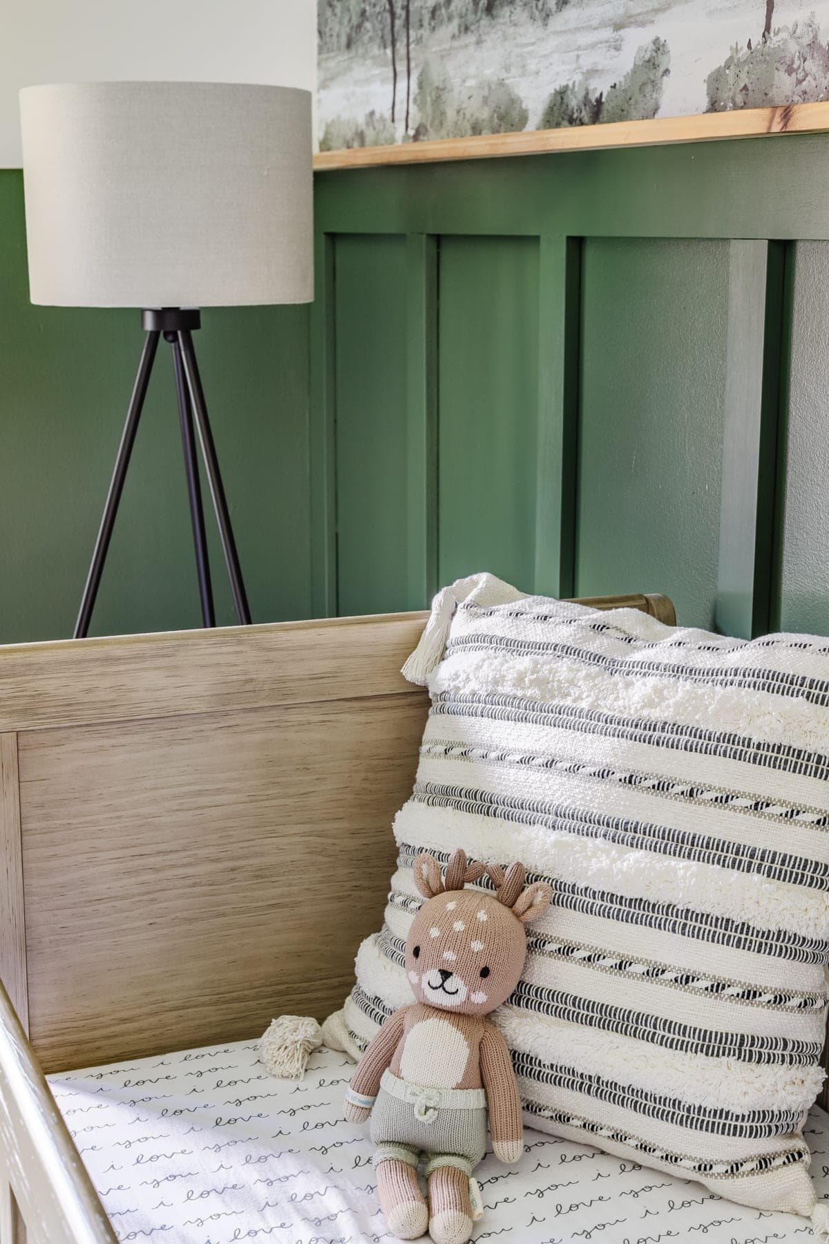 baby boy nursery with woodland theme - floor lamp and pillow with natural wood crib