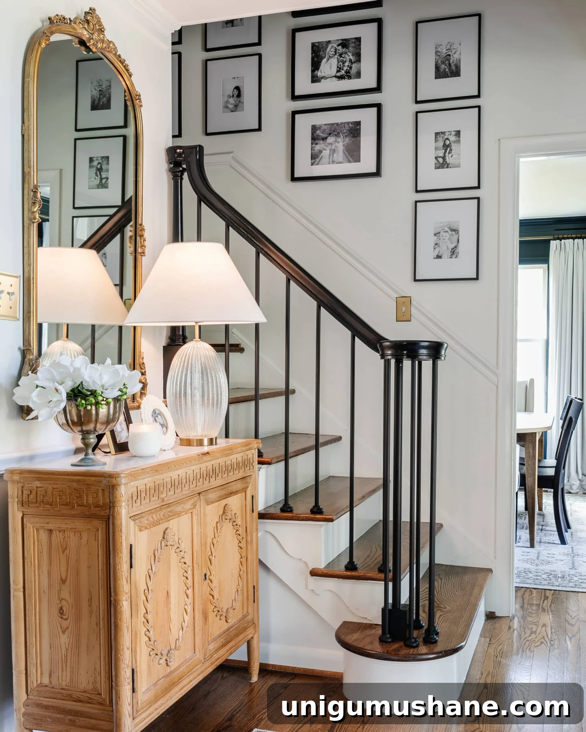 gallery wall on stairs in an entryway with accent chest, mirror, and lamp