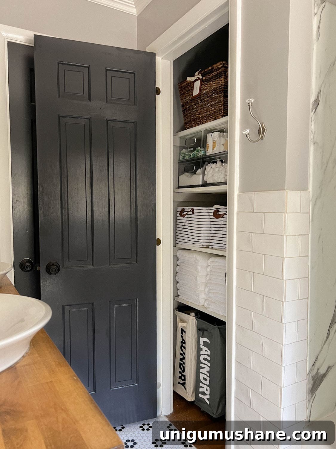 linen closet in a bathroom with black door, white tile, and gray walls