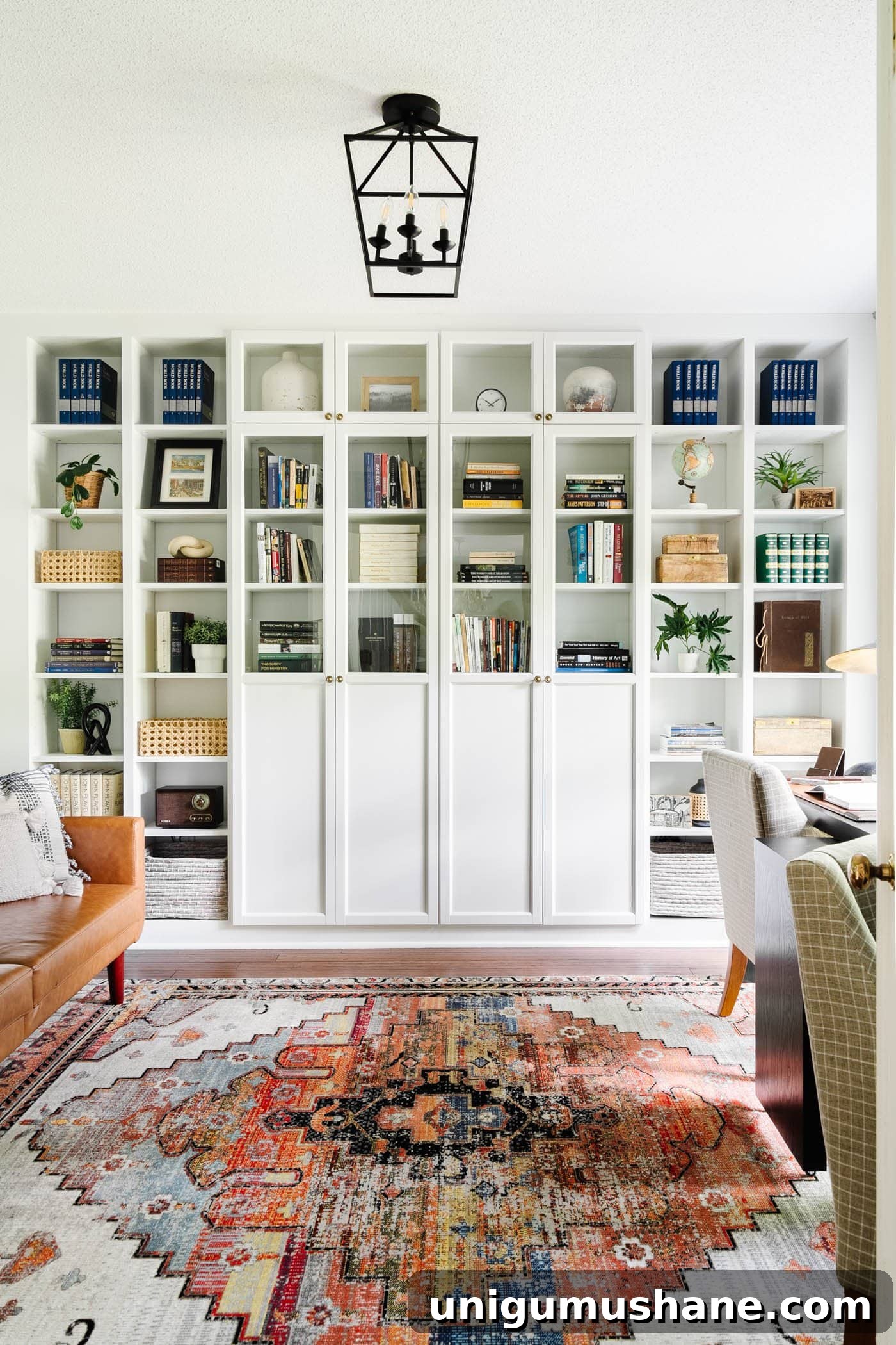 23 Small Room Tricks That Make Any Space Look Bigger 13 home office with white built-in bookshelves and glass front cabinets, futon, rug, and desk against a window