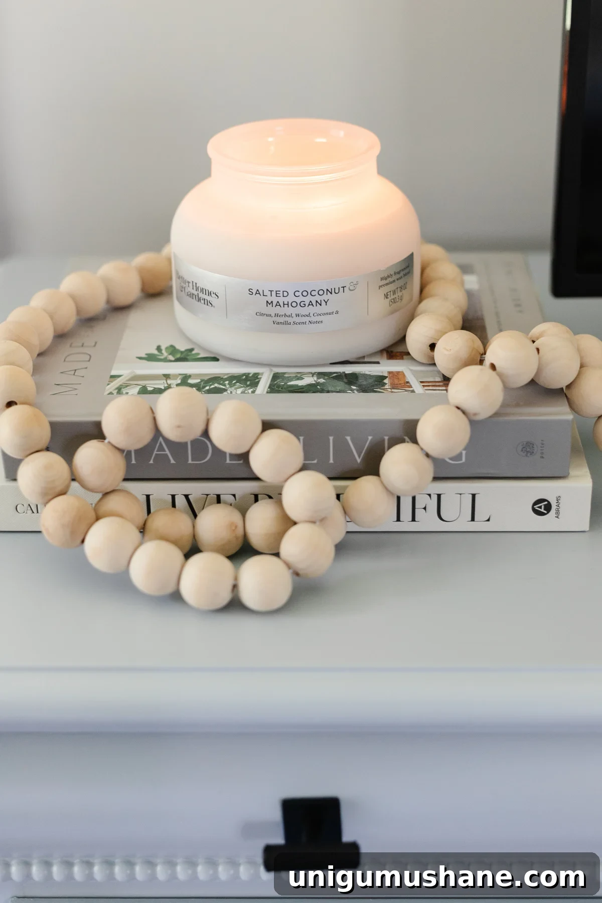 candle with wooden beads and book stack on dresser