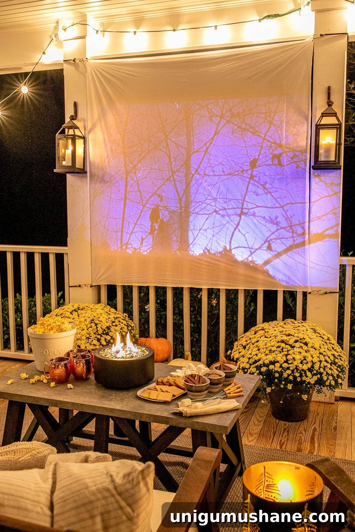 How to Host a Backyard Movie Night on a Budget 17 fall movie playing on an outdoor movie screen on a back porch decorated for fall with pumpkins, mums, and tabletop fire pit