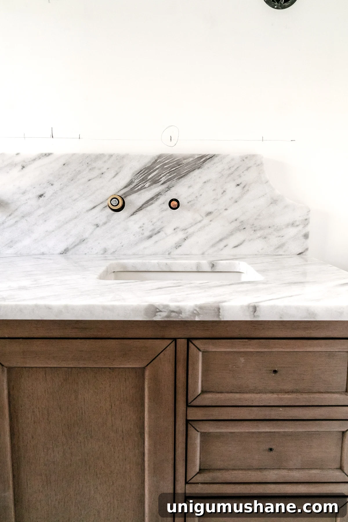 wood vanity with scalloped marble backsplash in a bathroom