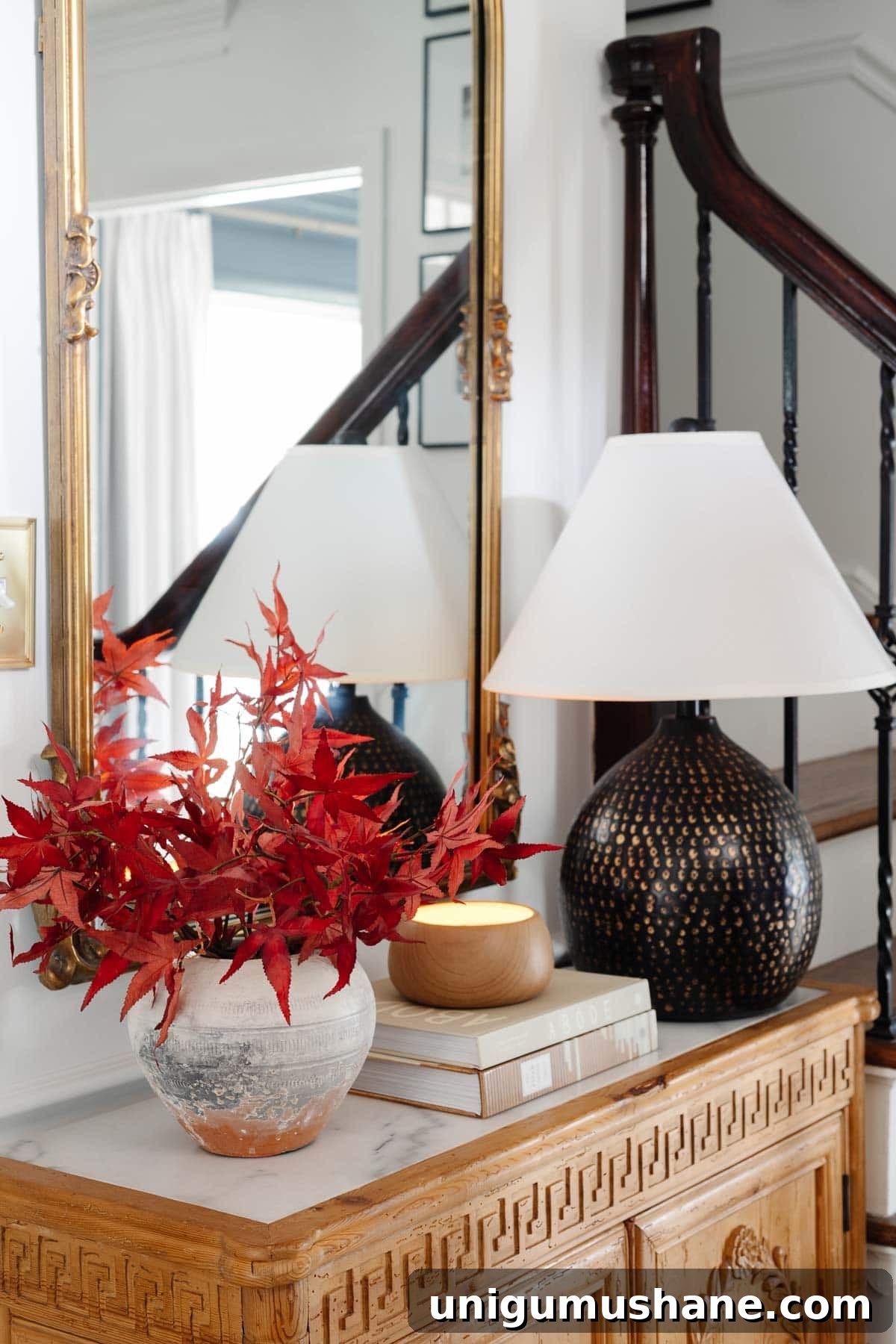marble top entryway table with mirror, lamp, and vase of fall leaves