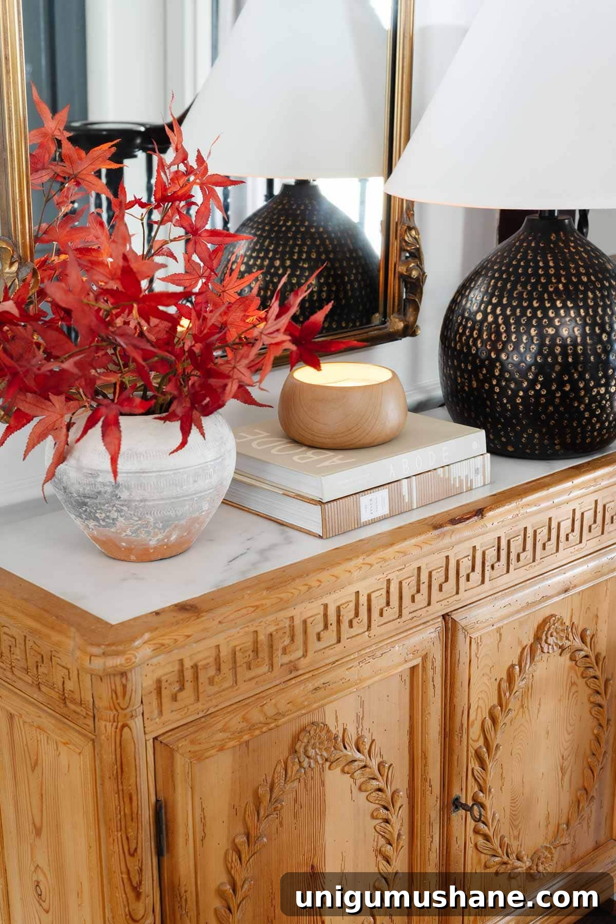 entryway table with mirror, lamp, and vase of fall leaves