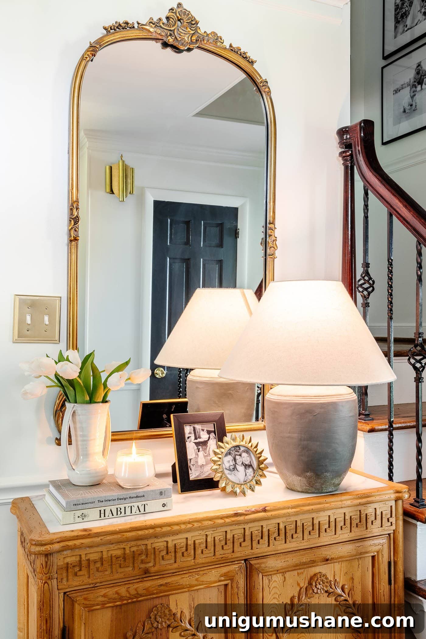 Style an Entry Table Like a Pro: Step-by-Step Guide 3 entry table decor in a foyer with gold mirror, lamp, vase of tulips, candle, and picture frames on a carved wood cabinet