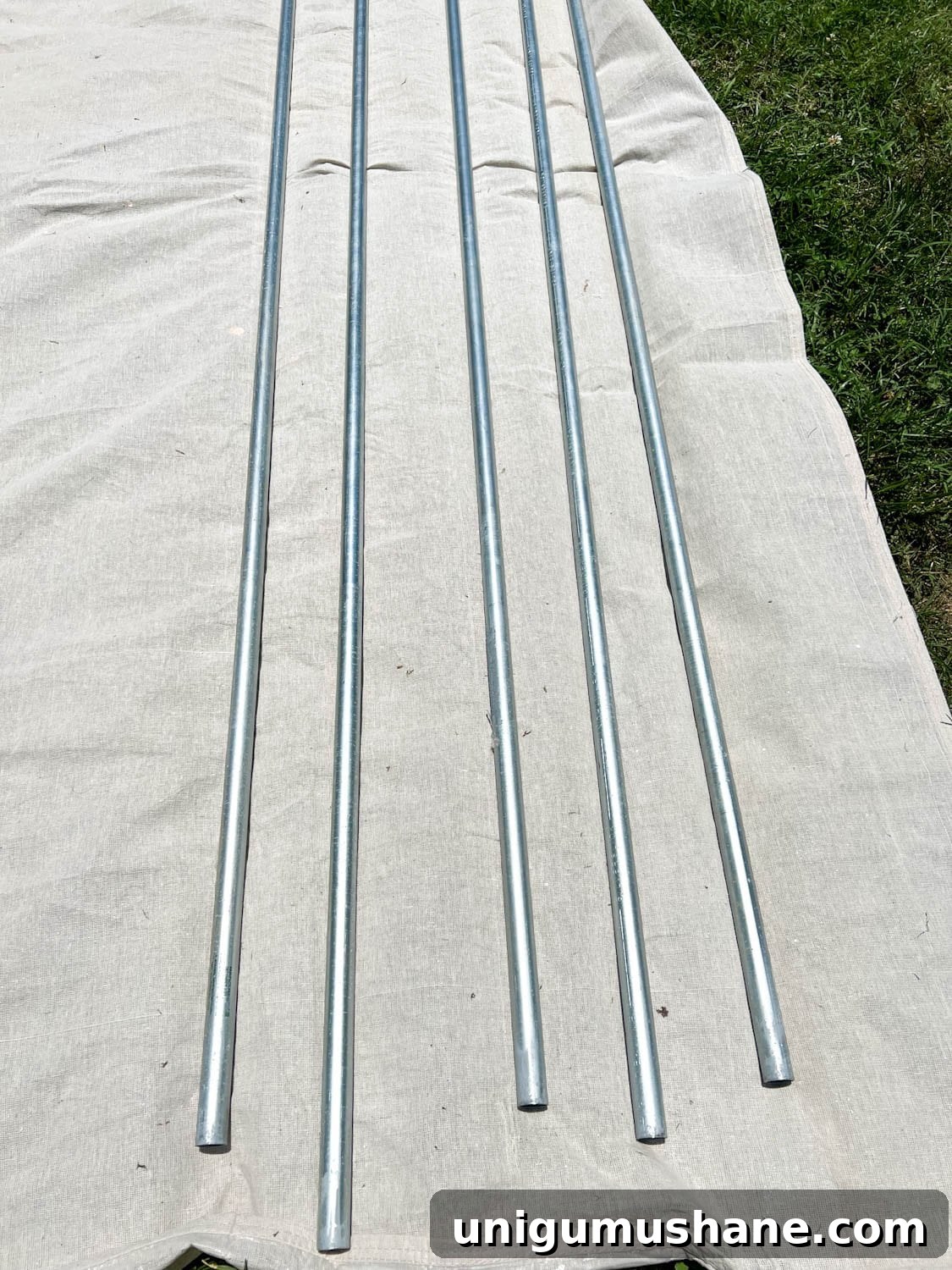 How to Hang Outdoor String Lights Anywhere in Your Backyard 10 conduit poles on a drop cloth ready to be painted