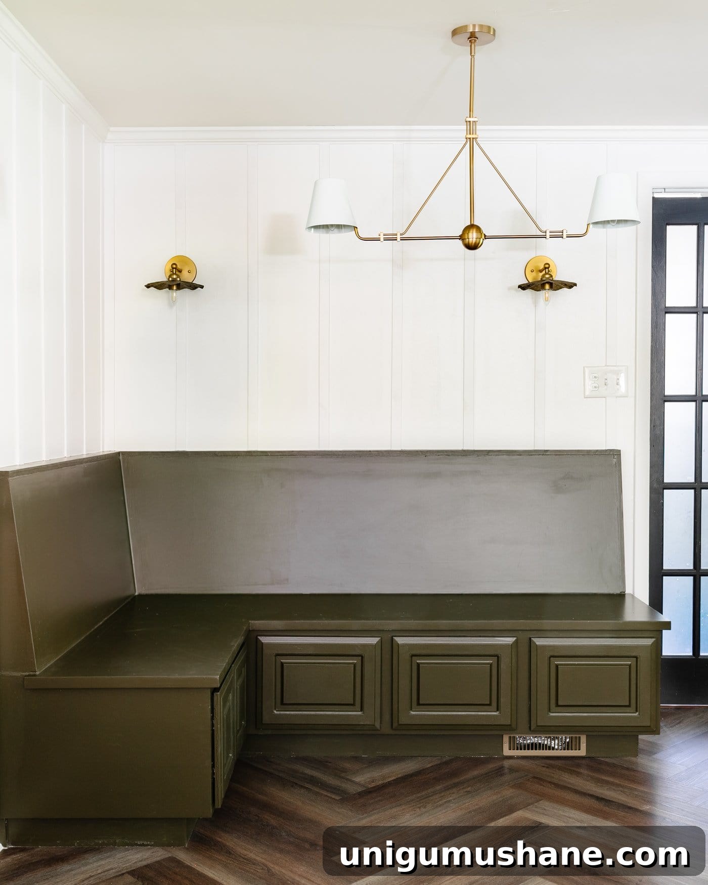 breakfast nook with green banquette bench, white batten wall made of lattice strips, and brass lighting