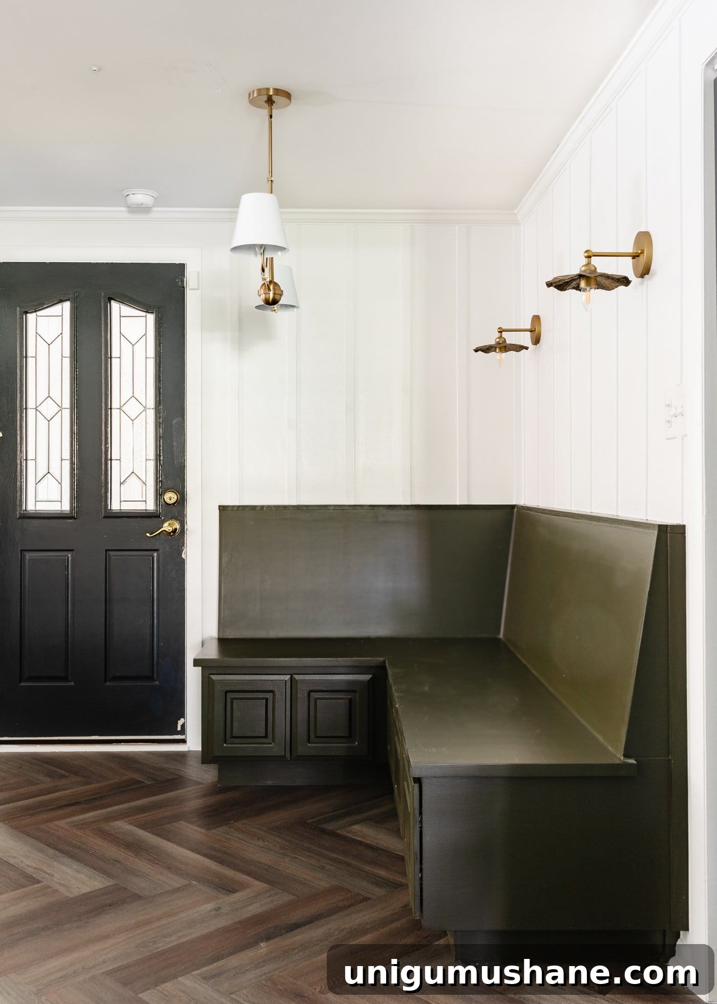 olive green banquette bench in a breakfast nook with white batten, herringbone floors, and black door