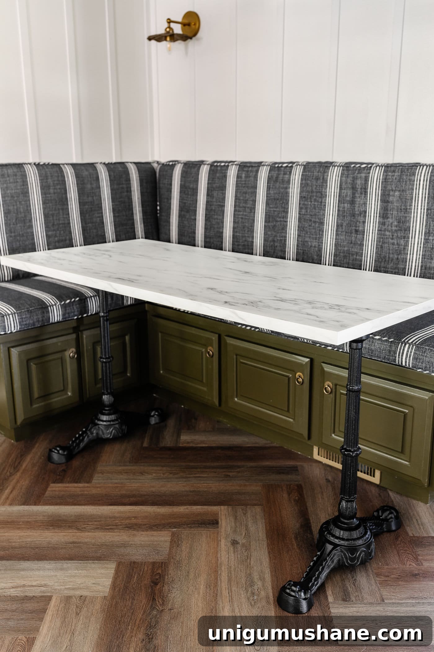 Parisian style faux marble dining table with cast iron pedestal legs against an olive green banquette with charcoal striped bench cushions and herringbone wood floors