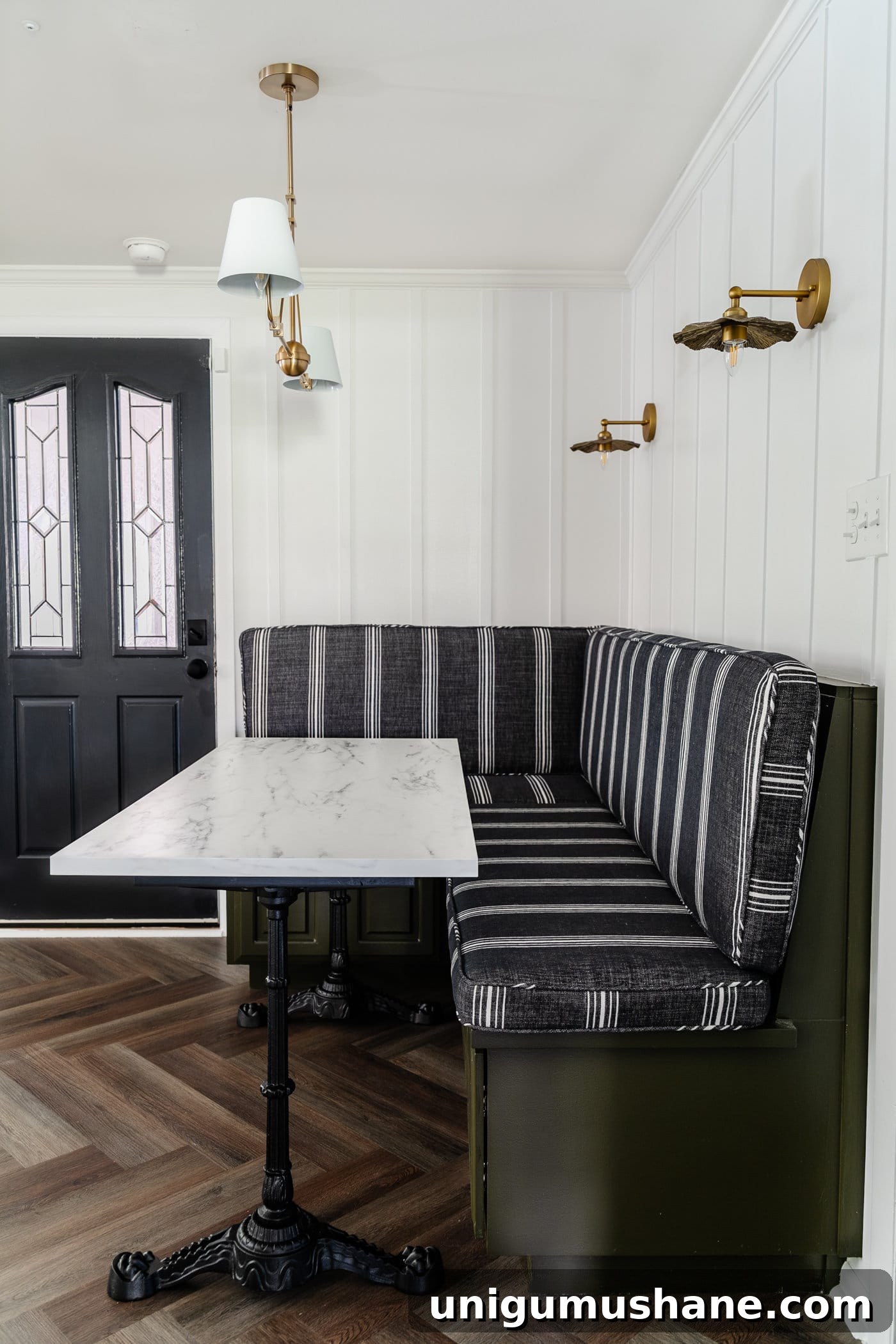 Parisian style faux marble dining table with cast iron pedestal legs against an olive green banquette with charcoal striped bench cushions and herringbone wood floors