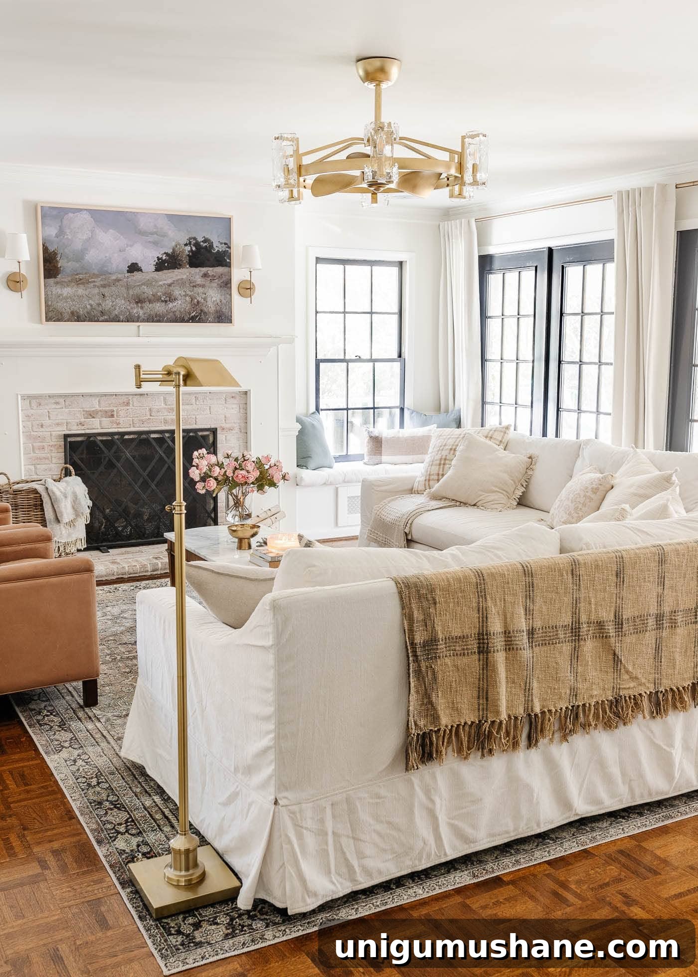 5-Year Home Transformation: Before and After Tour 24 white living room with limewashed brick fireplace, gold fandelier, white Pottery Barn sofas, leather recliners, art TV, and black French doors