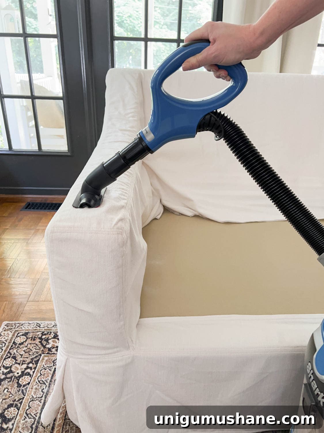 vacuuming sofa slipcover with wand attachment to remove hair, dirt, and lint