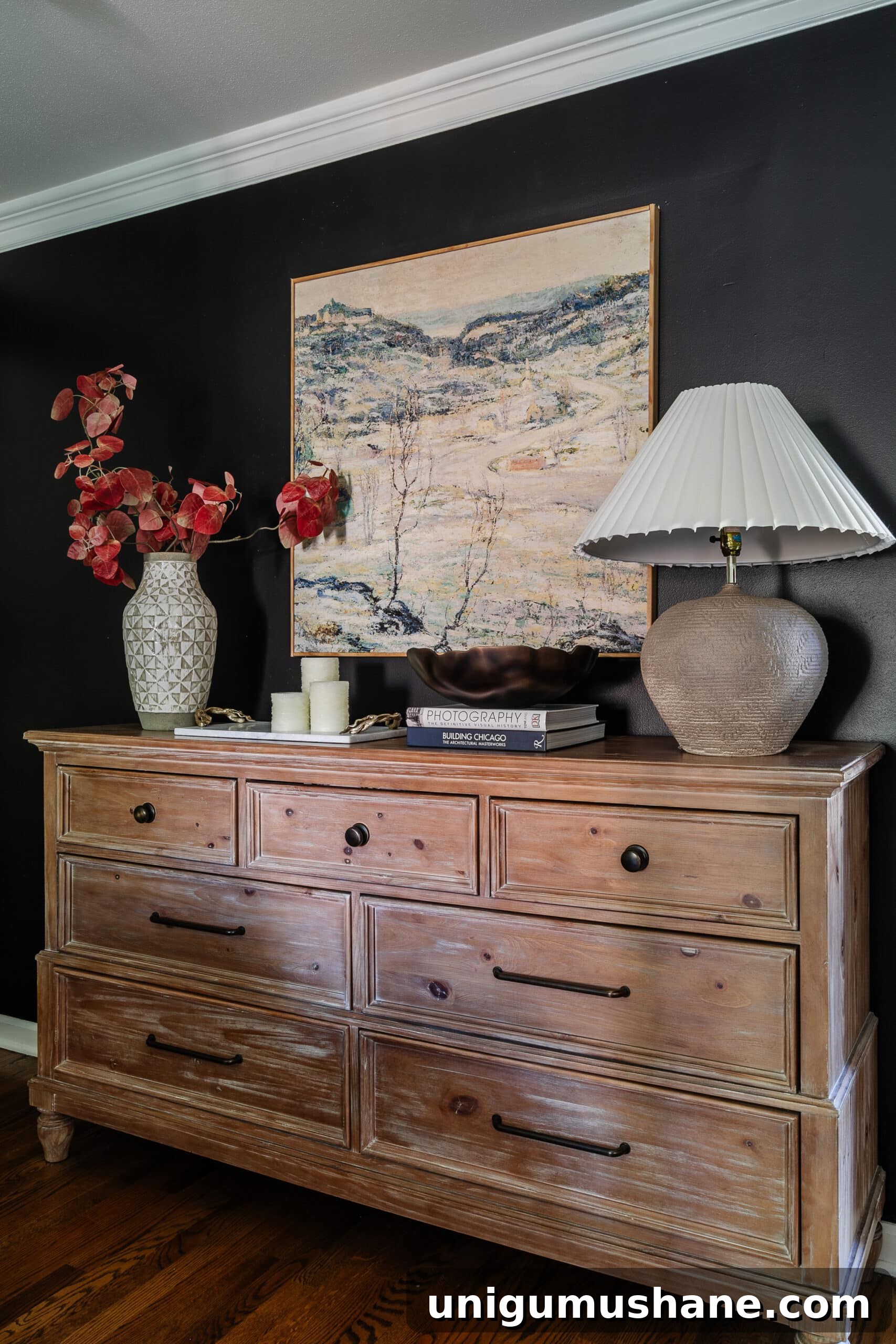 10 Affordable Cozy Bedroom Ideas to Improve Sleep 4 wood dresser with large wall art, vase of fall branches, and table lamp