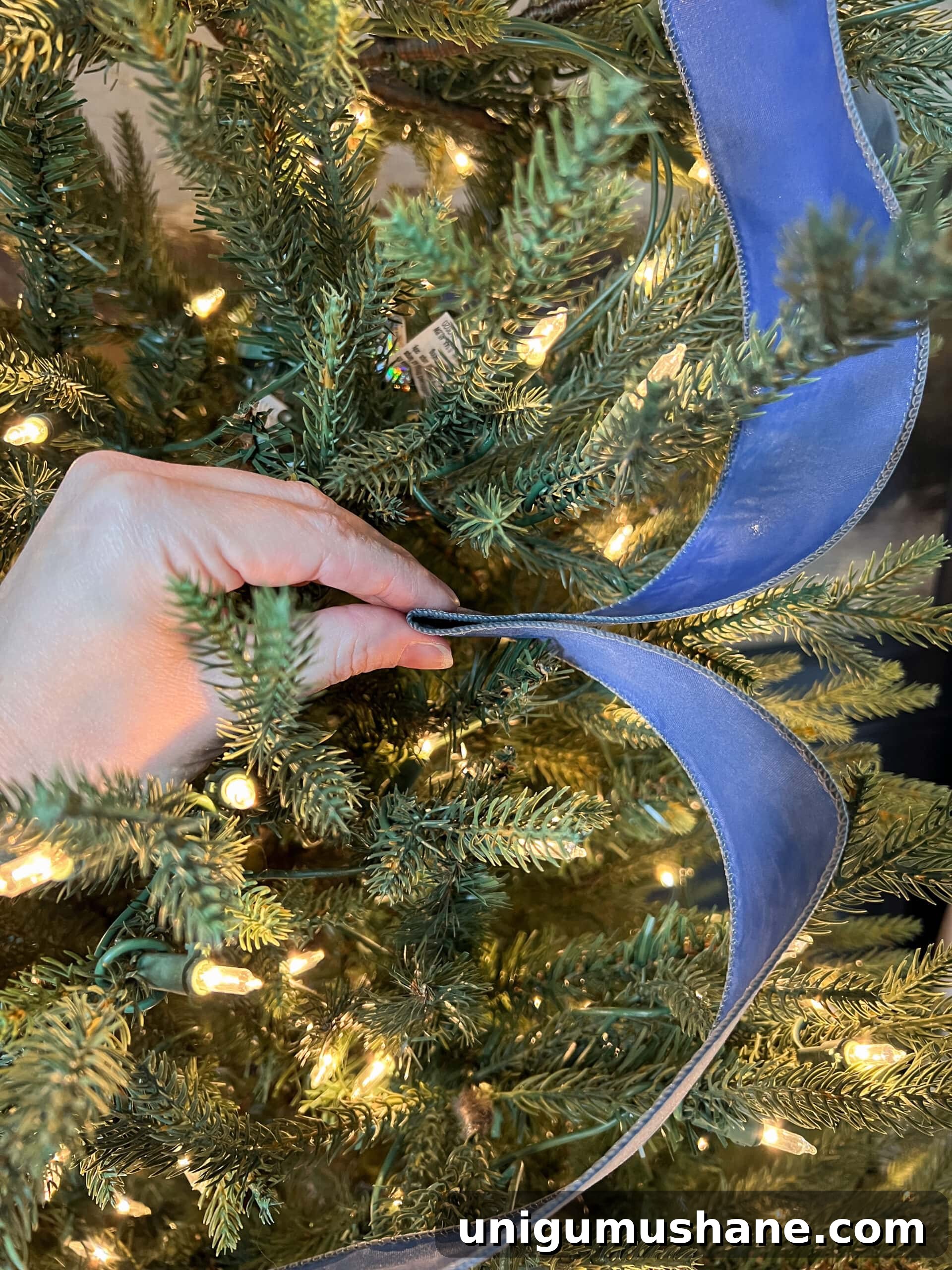 How to Add Ribbon Decorations to Your Christmas Tree 7 pinching middle of ribbon to tuck between branches