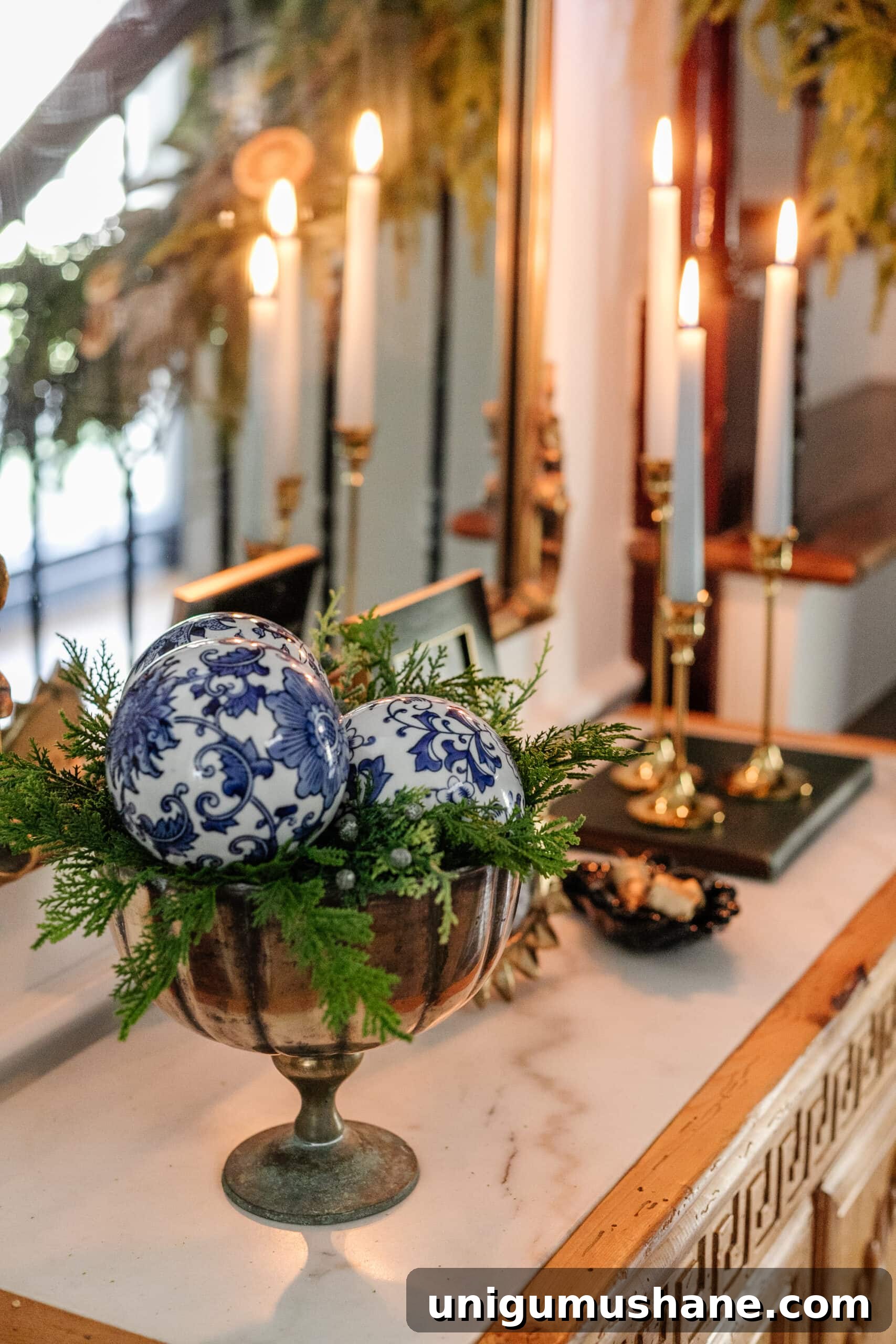 porcelain orbs in a footed bowl with greenery on an entryway table for blue and white Christmas decor