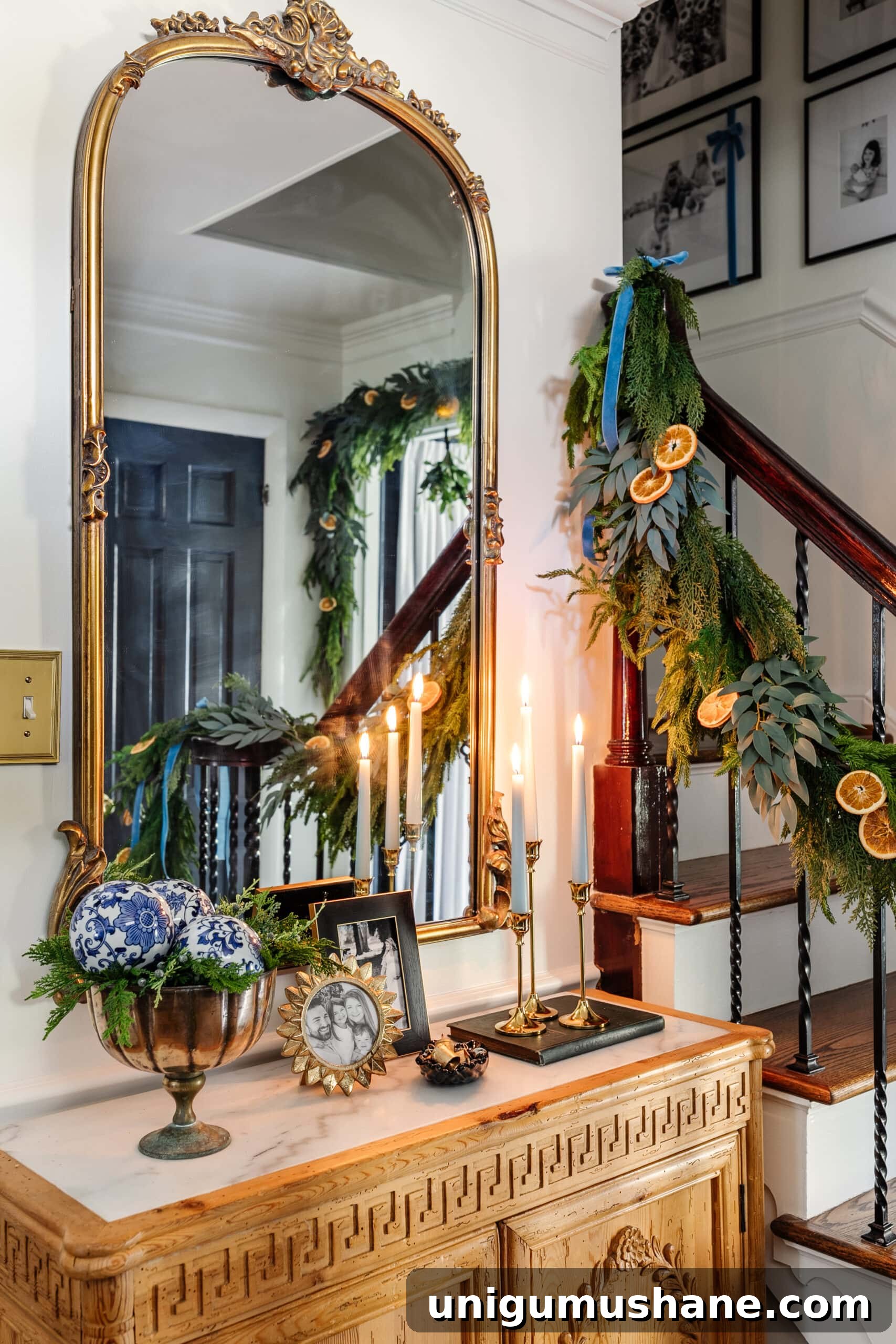 entryway Christmas decor on a table with candles, mirror, picture frames, and bowl of greenery