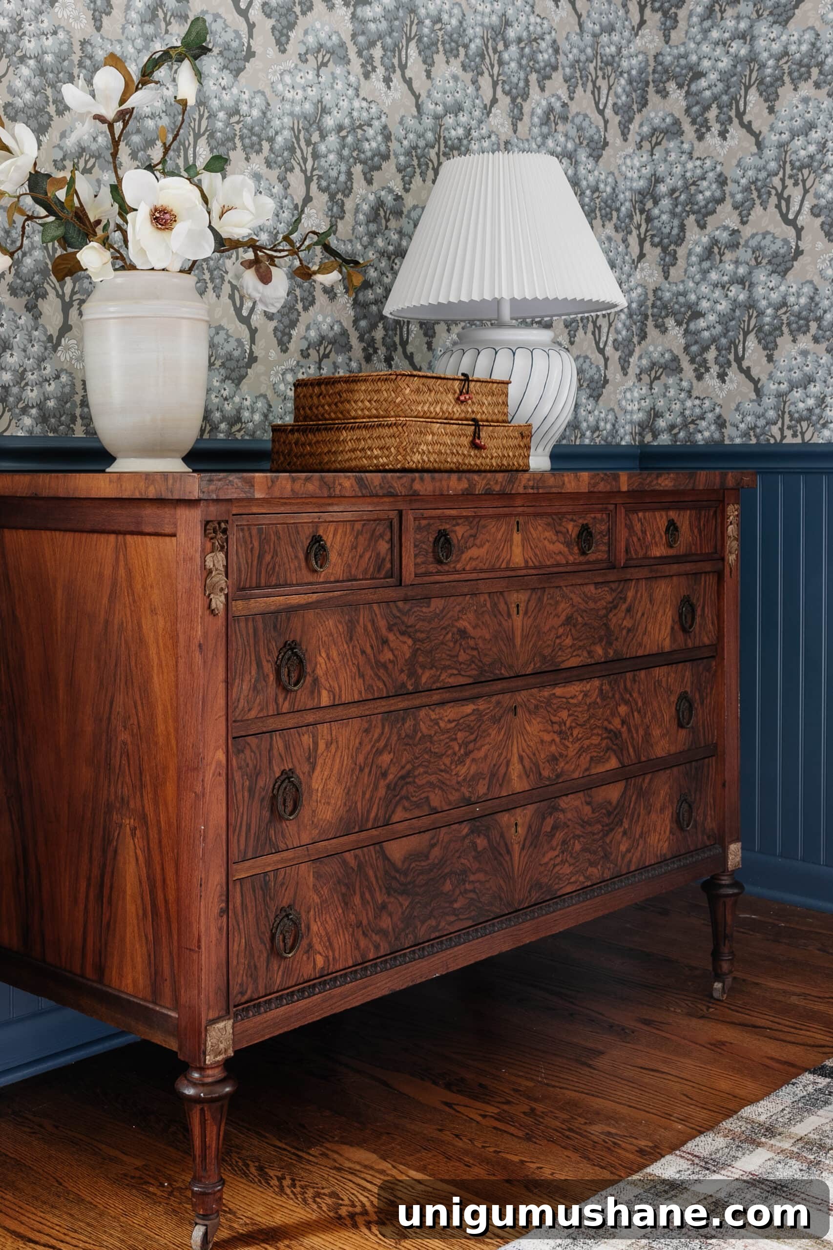 Burl Wood Furniture for Every Budget: Refinished Burl Dresser 5 burl wood dresser styled with vase of flowers woven basket boxes and lamp in a bedroom with blue vintage wallpaper