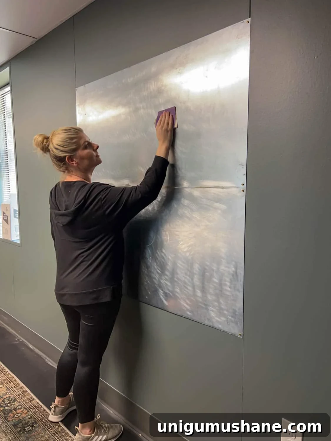 sanding metal sheets on a wall to apply a mural as DIY art